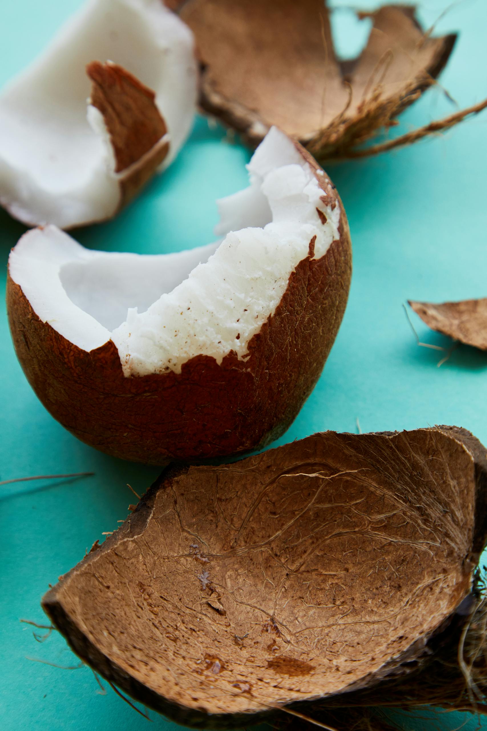 Close-up of a cracked coconut on a turquoise background, showcasing its natural texture and ripe pulp.
